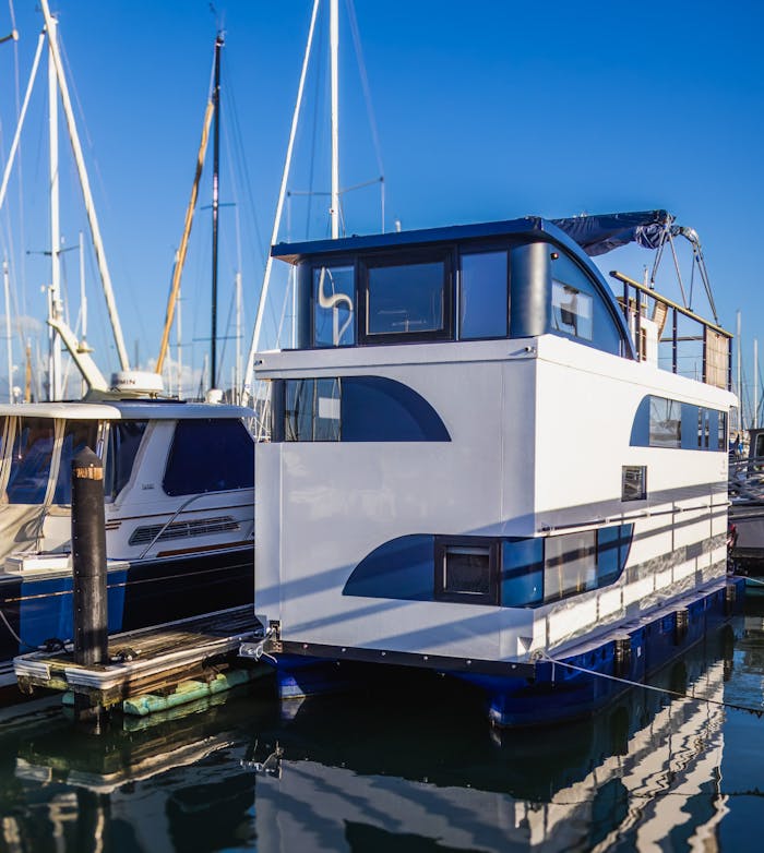 Modern houseboat docked at a marina under clear blue skies, reflecting on calm water.