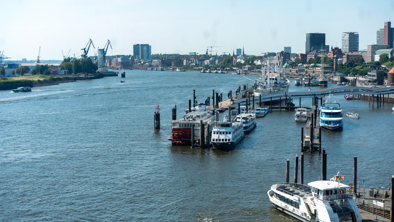 Aerial view of Hamburg harbor with boats and cityscape under clear blue skies.