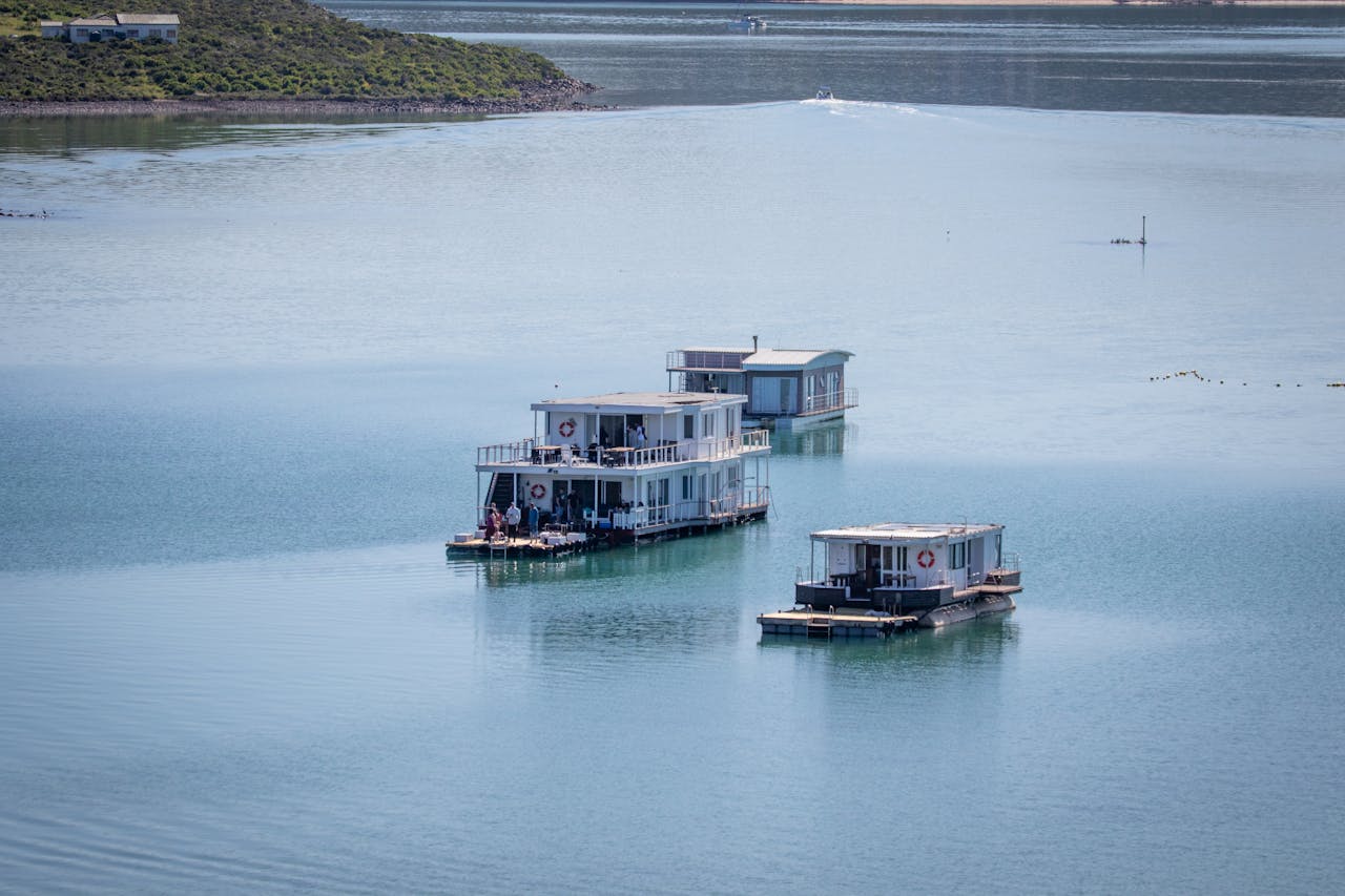 Three luxury houseboats float peacefully in the serene waters of Kraalbaai Lagoon, South Africa.